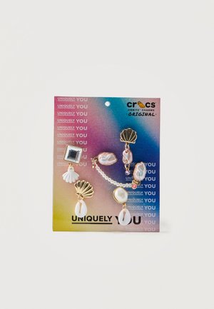 Cinque charm Crocs Jibbitz con design di conchiglie, perle e iridescenti su una scheda a gradiente colorato etichettata "Unicamente te."