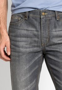 Jeans in denim grigio con una vestibilità slim, design a cinque tasche, cuciture a contrasto e chiusura con bottone classico in vita.