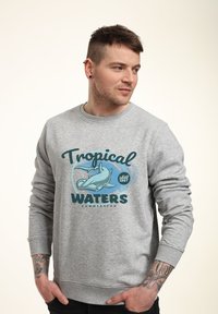 Felpa grigia con scollo rotondo, caratterizzata da una grafica di squalo martello blu e la scritta "Tropical Waters" in caratteri bold. Materiale in cotone.