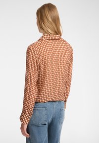 Camicia button-up in arancione ruggine, con un motivo a griglia in tonalità più chiare. Maniche lunghe, design con colletto, realizzata in tessuto liscio. Abbinata a jeans blu.