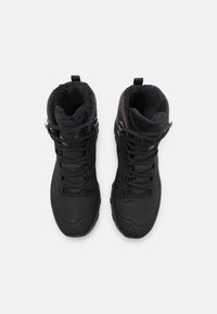 Ett par svarta isolerade vandringskängor med snörning, fleecefoder och dragflikar, visade uppifrån på en vit bakgrund.