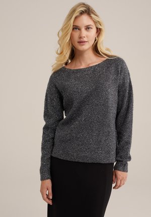 Grauer, glitzernder Strickpullover mit weitem Rundhalsausschnitt, langen Ärmeln und gerippten Bündchen, kombiniert mit einem schwarzen Rock in einem minimalistischen Setting.