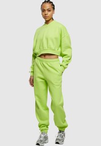 Felpa corta verde neon con scollo a V e pantaloni jogger a vita alta abbinati, entrambi in morbido tessuto con polsini e vita elastici.