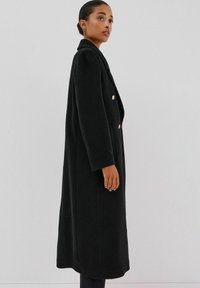 Kaksirivinen musta takki, joka on valmistettu teksturoidusta kankaasta, ja siinä on kultaiset napit, notchettu kaulus ja sivutaskut. Keskipitkä malli.