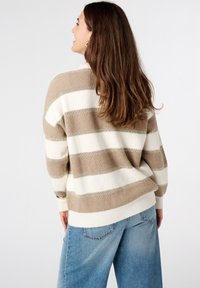 Beige en witte gestreepte trui met een relaxte pasvorm, geribbelde textuur en verlaagde schouders. Gecombineerd met lichtblauwe spijkerbroek.