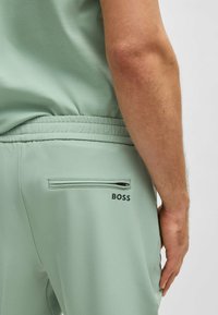 Mintgroene jogger shorts met een elastische tailleband, zijzakken en een met rits afsluitbare achterzak met een zwart "BOSS" logo. Soepele textuur.