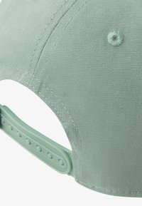Casquette en tissu vert avec une surface texturée, des détails de couture, et une sangle ajustable en plastique à l'arrière avec des trous ronds pour le réglage.