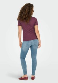 Lila gerippte T-Shirt, taillierte Passform mit kurzen Ärmeln, kombiniert mit hellblauen Skinny Jeans. Modell trägt rote Ballerinas, von hinten betrachtet.