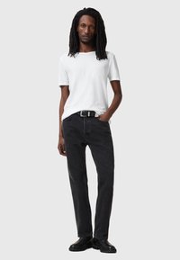 T-shirt bianco a maniche corte abbinato a jeans in denim neri e una cintura nera. I jeans hanno una vestibilità dritta e una leggera scoloritura. Stivali neri completano il look.