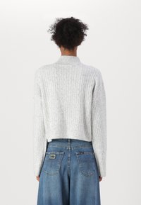 Kuttet grå genser med kabelstrikk mønster og høy krage, parret med blå høy midje denimbukser med baklommer.