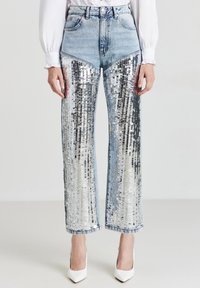 I pantaloni in denim presentano lati con paillettes e una texture riflettente argentea, un design a gamba dritta, vita alta e denim blu a contrasto nella parte superiore.