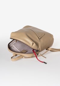 Beige leren rugzak met ritsluiting, voorzien van een gevoerde binnenkant met patroon en een rode stoffen trekband. Gladde textuur en minimalistisches ontwerp.