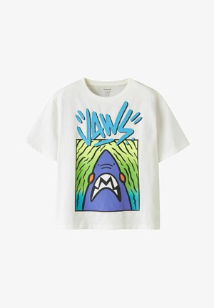 T-shirt blanc avec un requin de dessin animé bleu à la bouche ouverte sous le texte stylisé "JAWS" en bleu sur un fond vert et bleu.
