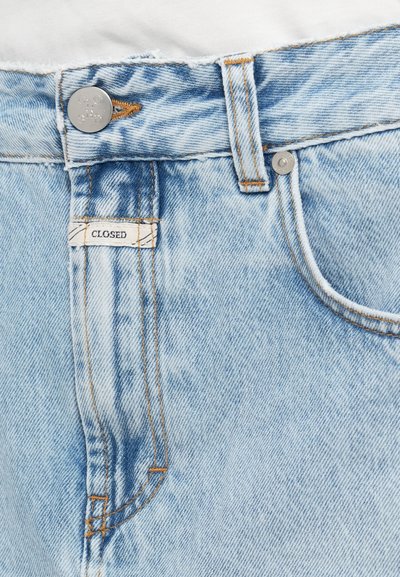 Φωτεινό μπλε τζιν με ξεφτισμένο τελείωμα, πορτοκαλί ραφές και ασημένιο κουμπί κλεισίματος. Η ετικέτα της μάρκας γράφει "CLOSED".