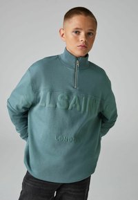 Žalias džemperis su aukštu apykakle ir pusiau užtrauktuku. Priekyje yra iškeltas logotipas "ALLSAINTS" ir "LONDON". Minkšta tekstūra, atsipalaidavęs siluetas.