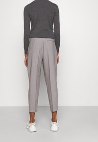 Grå sweater med lange ærmer, kombineret med lysegrå plisserede bukser. Bukserne har smalle ben og en baglomme. Hvid sneakers fuldender looket.