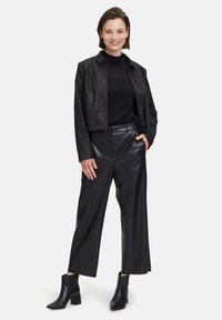 Schwarze, verkürzte Jacke mit strukturiertem Muster, kombiniert mit hoch geschnittenen schwarzen Lederimitat-Hosen und Ankle Boots mit Blockabsatz.