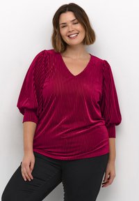 Top magenta à col en V avec texture en côtes verticales, manches ballon et coupe décontractée, associé à un pantalon noir ajusté.