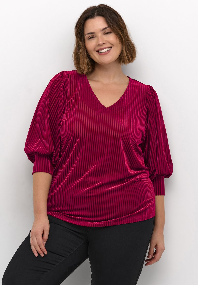 Top magenta à col en V avec texture en côtes verticales, manches ballon et coupe décontractée, associé à un pantalon noir ajusté.