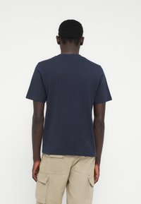 Μπλε ναυτικό κοντομάνικο μπλουζάκι με λαιμόκοψη, κατασκευασμένο από απαλό ύφασμα, εμφανίζεται από πίσω. Χωρίς ορατά λογότυπα.