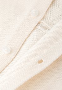 Cárdigan de punto color crema con botones grandes, patrones texturizados y un pequeño agujero en forma de corazón en la tela.