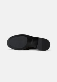 Black shoe sole with smooth rubber material, slightly raised heel, and horizontal ridges on the back for traction. “Vagabond” branding present.