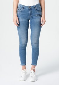 Lichtblauwe skinny jeans van denim. Kenmerken zijn onder andere voorzakken, een rits en een knoopsluiting. Gepaard met witte sneakers.
