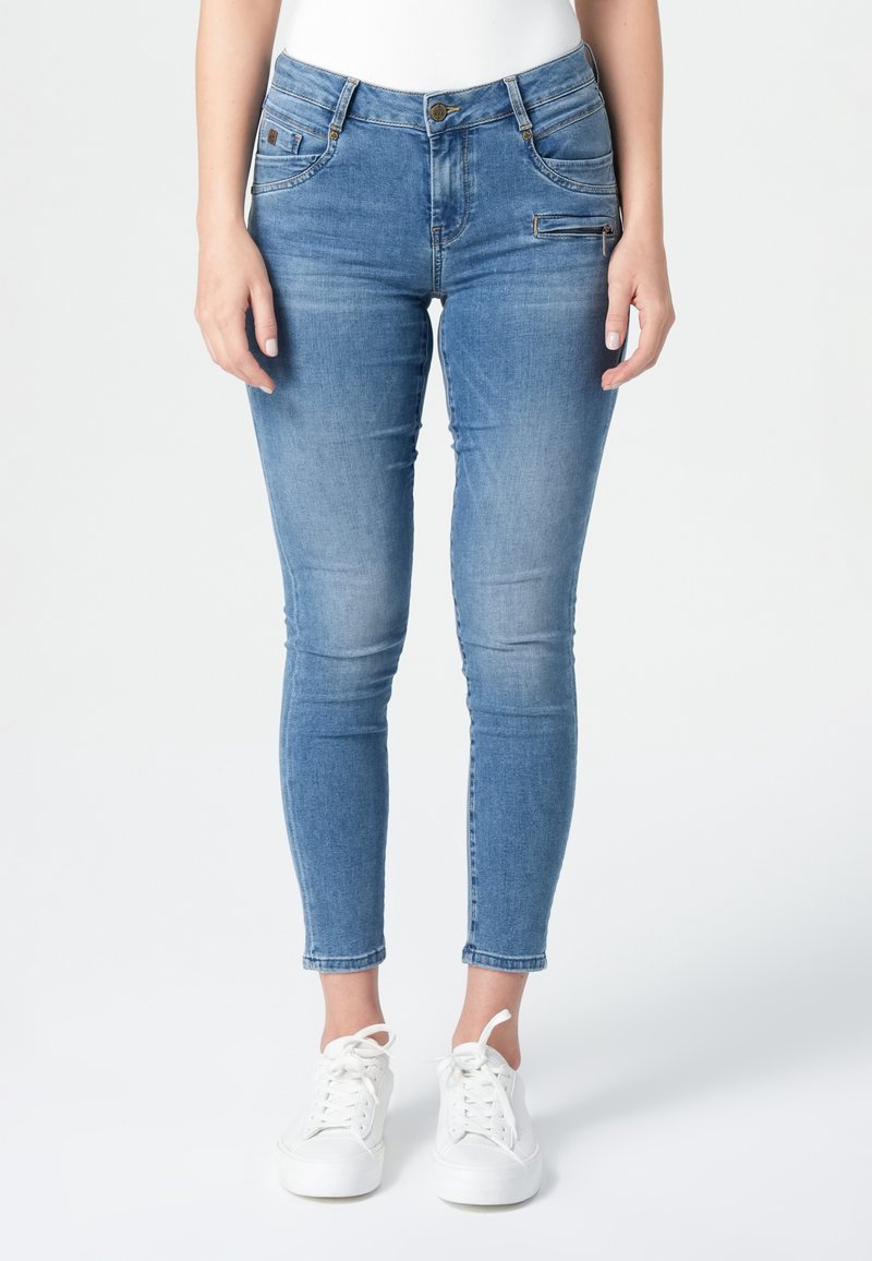 Lichtblauwe skinny jeans van denim. Kenmerken zijn onder andere voorzakken, een rits en een knoopsluiting. Gepaard met witte sneakers.