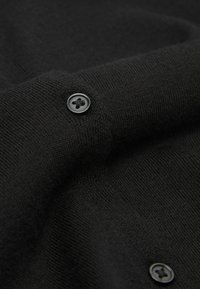 Schwarzer Strickpulloverstoff mit glatter Textur, ausgestattet mit einem schwarzen Knopf im Vierlochdesign. Betont das weiche, gleichmäßige Strickmuster.