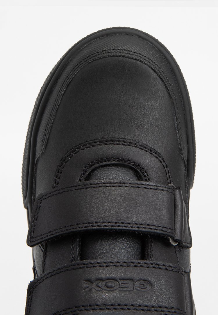 Las zapatillas de cuero negro cuentan con una puntera redondeada, dos correas de Velcro, costuras decorativas y acentos texturizados en los laterales.