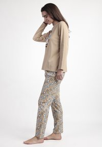 Camiseta de manga larga beige con diseño gráfico, combinada con pantalones ligeros beige que presentan personajes de dibujos animados azules y un patrón de texto, ambos de algodón.