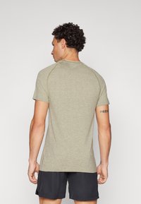 Ανοιχτό ελαιοπράσινο κοντομάνικο πουκάμισο με υφή, στρογγυλή λαιμόκοψη και ράγλαν μανίκια; φοριέται με μαύρη βερμούδα.