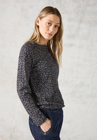 Haut à manches longues noir avec des motifs tourbillonnants blancs, encolure ronde et tissu texturé, associé à un pantalon en denim foncé.