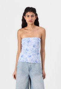 Top azzurro chiaro senza spalline con stampa floreale, realizzato in tessuto morbido. Caratterizzato da un design aderente e una texture liscia. Abbinato a jeans a gamba larga azzurri chiari.
