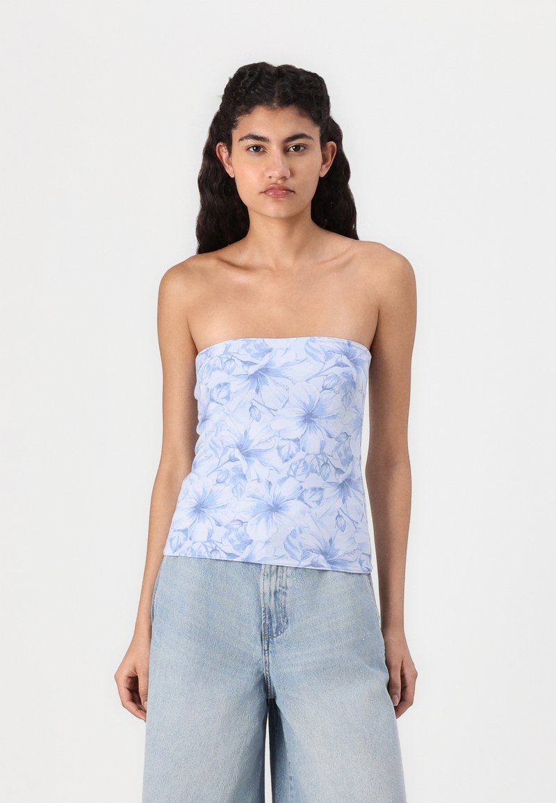 Top azzurro chiaro senza spalline con stampa floreale, realizzato in tessuto morbido. Caratterizzato da un design aderente e una texture liscia. Abbinato a jeans a gamba larga azzurri chiari.