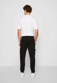 Svarta cargo-byxor med flera fickor, elastiska muddar, kombinerat med en enkel vit t-shirt i bomull och vita sneakers.