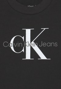 Czarny bawełniany t-shirt z dużym białym logo "CK" oraz napisem "Calvin Klein Jeans" w nowoczesnej czcionce bezszeryfowej. Krótki, okrągły dekolt.