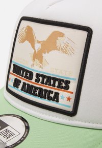 Weiße Kappe mit einem beigen und goldenen Adler-Graphic, schwarzem Rand und dem Text "OREGON STATE UNITED STATES OF AMERICA", mit einem grünen Schirm.