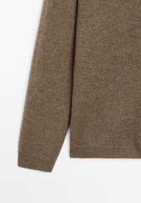 Brązowy sweter wykonany na drutach, charakteryzujący się miękką teksturą, długimi rękawami i ściągaczem u dołu. Wyraźne, równe szycie w całym materiale.