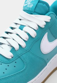 Mäkké zelené tenisky Nike Air Force 1 s bielymi šnúrkami, z semišových a kožených materiálov, okrúhlou špičkou a vyčnievajúcim bielym logom na boku.