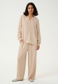 Beiger zweiseitiger Freizeitanzug bestehend aus einem Langarmshirt mit einem geknöpften Henley-Ausschnitt und weit geschnittenen Hosen, gefertigt aus weichem, glattem Stoff.