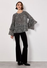 Zwart-wit geblokte blouse met uitlopende lange mouwen, ronde halslijn en een losse pasvorm, gecombineerd met zwarte uitlopende broek en enkellaarsjes.