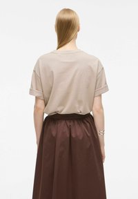 Beżowy, oversize T-shirt z podwiniętymi rękawami, połączony z brązową spódnicą plisowaną. Gładka struktura materiału; prosty, swobodny design.