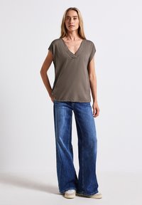 Top corto de color verde oliva, con un escote en V profundo, combinado con jeans de mezclilla azul de pierna ancha. La tela parece suave con una textura mínima.