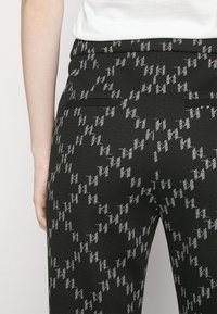 Černé kalhoty s potiskem, které mají strukturovaný design se stříbrnými akcenty, dvě zadní kapsy a přiléhající pas.