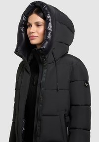 Doudoune noire avec une grande capuche pliable. Comprend un design matelassé, un revêtement intérieur brillant et une fermeture éclair à l'avant avec des boutons.