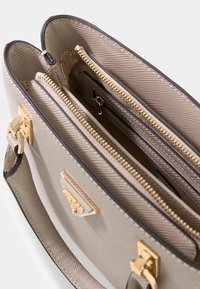 Beżowa, strukturalna torebka o fakturowanej powierzchni, z pozłacanymi elementami, dwoma komorami na zamek i małą kieszonką wewnętrzną.