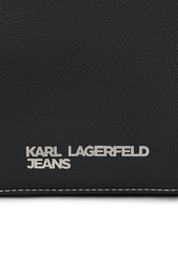 Portefeuille en cuir noir avec une finition texturée, des coutures blanches et un logo argenté en relief portant la mention "KARL LAGERFELD JEANS".