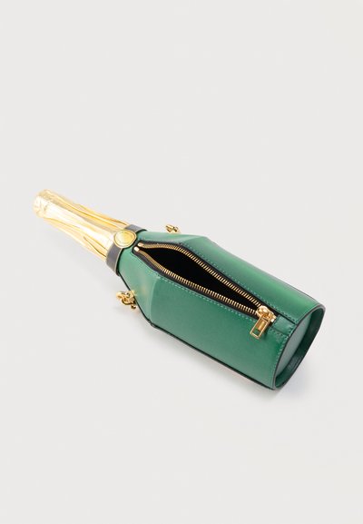 Πράσινη τσάντα χειρός σε σχήμα μπουκαλιού σαμπάνιας με χρυστό φερμουάρ και λεπτομέρεια για το λαιμό του μπουκαλιού τυλιγμένο με φύλλο αλουμινίου σε λευκό φόντο.