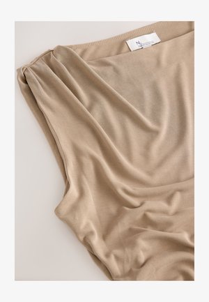 Beżowa, miękka tkanina ułożona swobodnie. Gładka tekstura z delikatnym połyskiem i subtelnymi fałdami. Metka widoczna na górnej krawędzi.